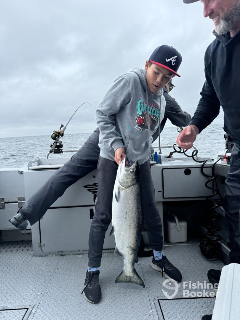 A young angler excitedly holds a large Salmon on a fishing boat, showcasing a successful catch during a fishing trip.
