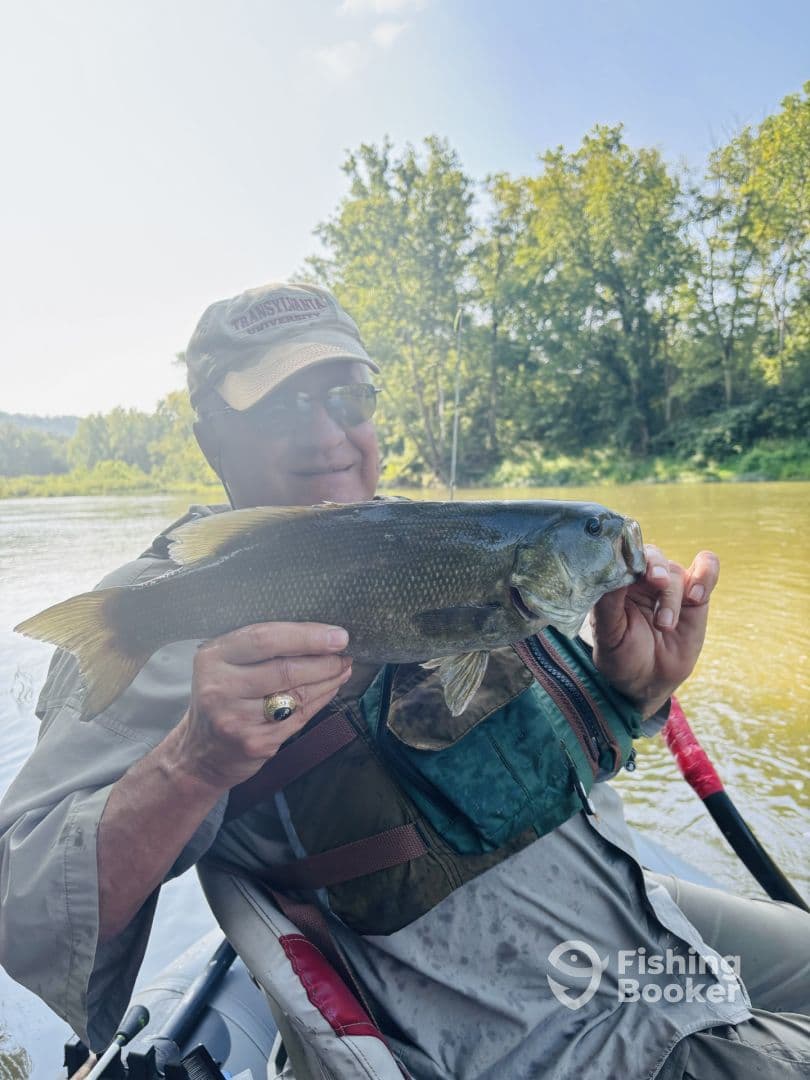 An angler proudly displaying a large Largemouth Bass while seated in a kayak on a serene river.