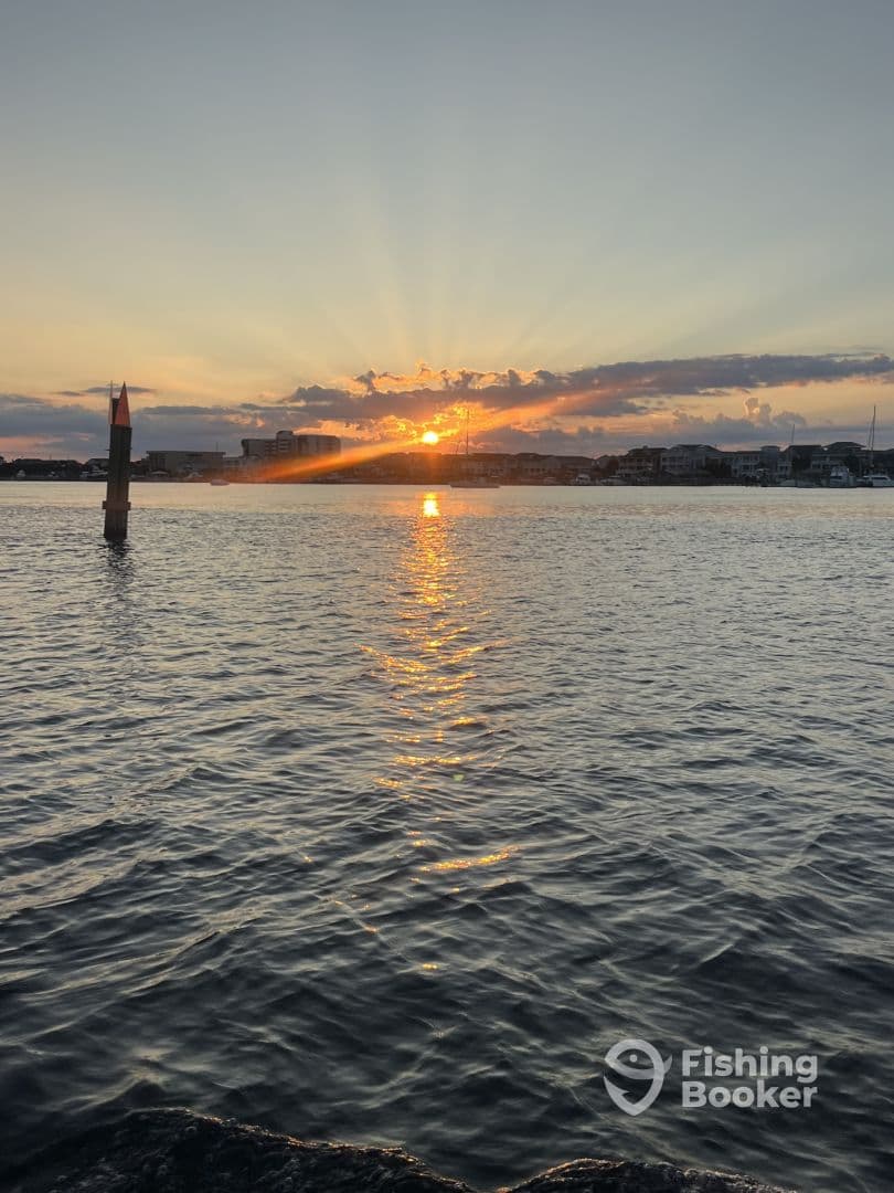 A serene sunset over the water, showcasing the reflection on the surface with a distant view of buildings and boats.