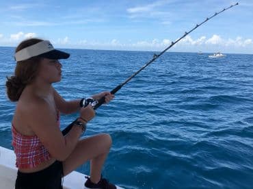 A young angler engaged in fishing on a sunny day, casting from a boat in open waters.