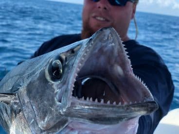 Angler proudly displaying a large fish, likely a King Mackerel, while out on the open water.