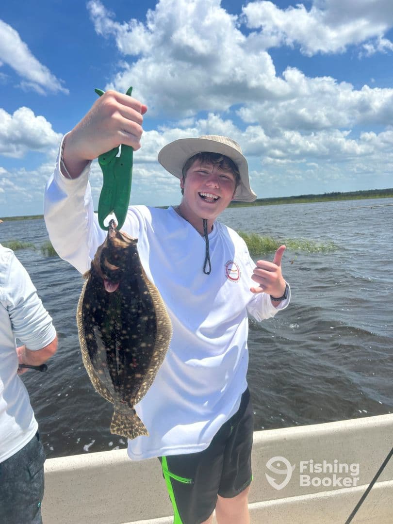 A young angler joyfully displaying a Flounder while fishing in a scenic waterway, showcasing a fun day on the water.