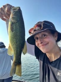 An angler proudly displaying a large Largemouth Bass while fishing on a serene lake.