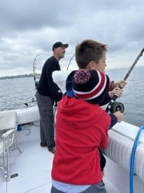 Two young anglers actively reeling in a fish while fishing on a boat, showcasing a family-friendly fishing experience.