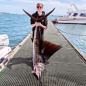An angler proudly displaying a large Sailfish on the dock, showcasing a successful deep-sea fishing trip.