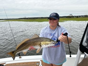 Angler holding a large Redfish while fishing in a scenic coastal environment.