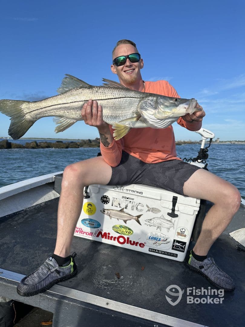Angler proudly displaying a large Striped Bass while seated on a fishing boat, showcasing a sunny day on the water.