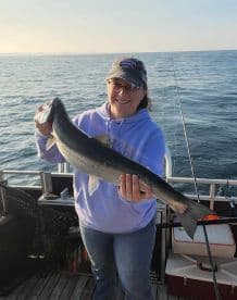 An angler proudly displaying a large Lake Trout while fishing on a calm lake, showcasing a successful day on the water.