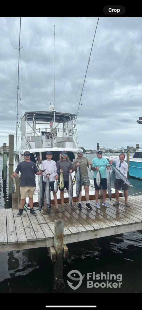 A group of anglers proudly displaying their catch of Mahi Mahi and King Mackerel on the dock after a successful fishing trip.