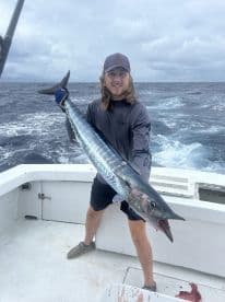 Angler proudly displaying a large Wahoo while fishing offshore, showcasing the excitement of a successful catch.