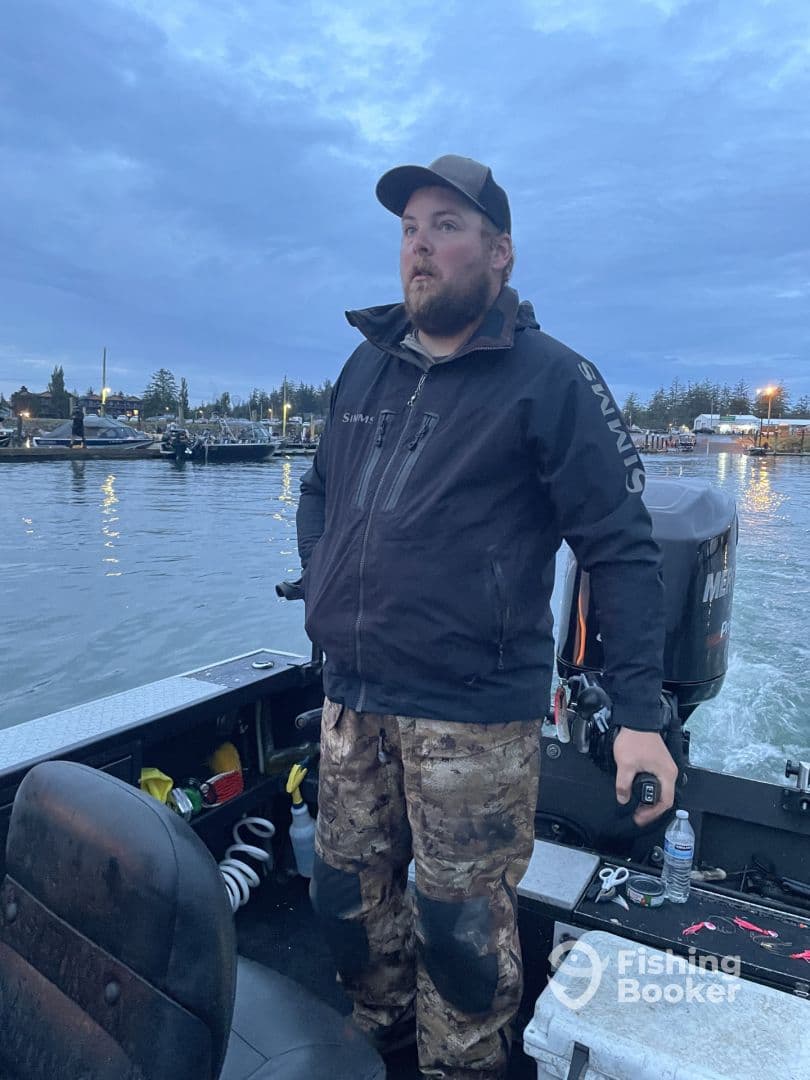 A fisherman stands at the helm of a boat, navigating through calm waters during twilight, showcasing the boat's interior and equipment.