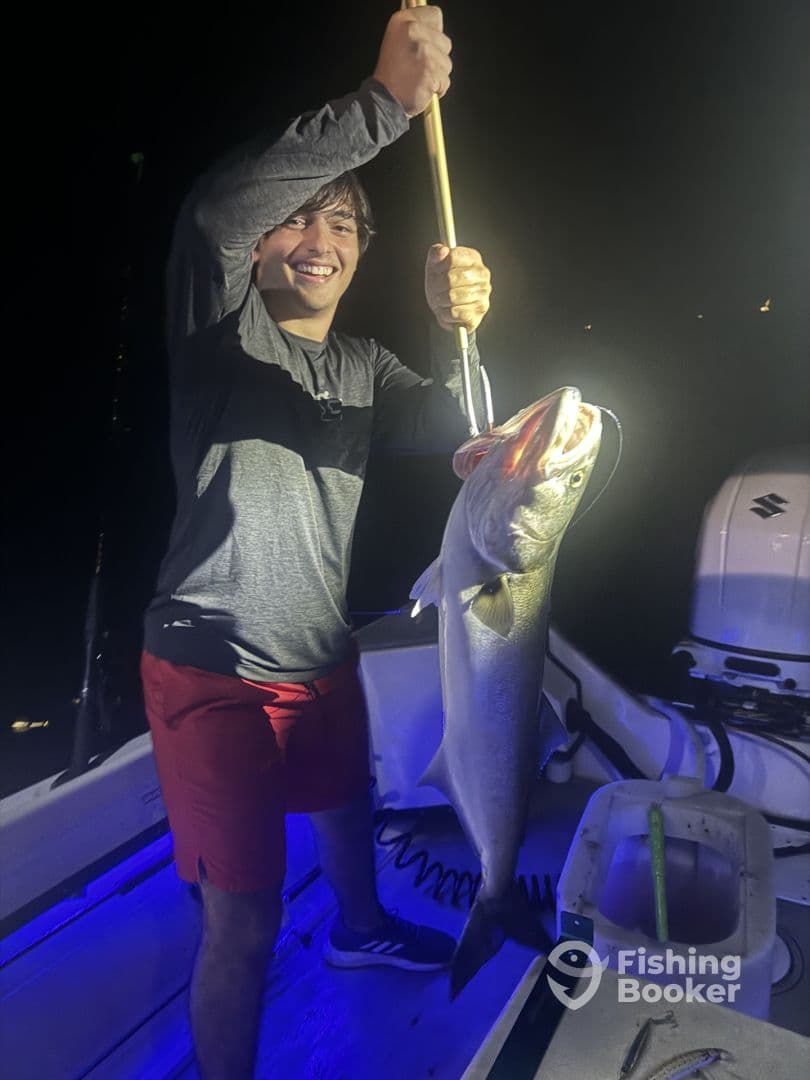 A young angler proudly displaying a large Snook caught during a night fishing trip on a boat.