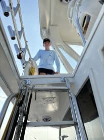A young angler smiling from the helm of a fishing boat, showcasing the interior layout and equipment.