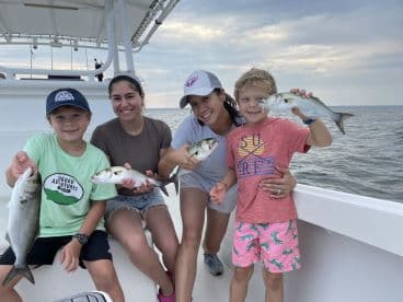 A family enjoying a successful fishing trip, showcasing their catch of multiple fish on a boat.