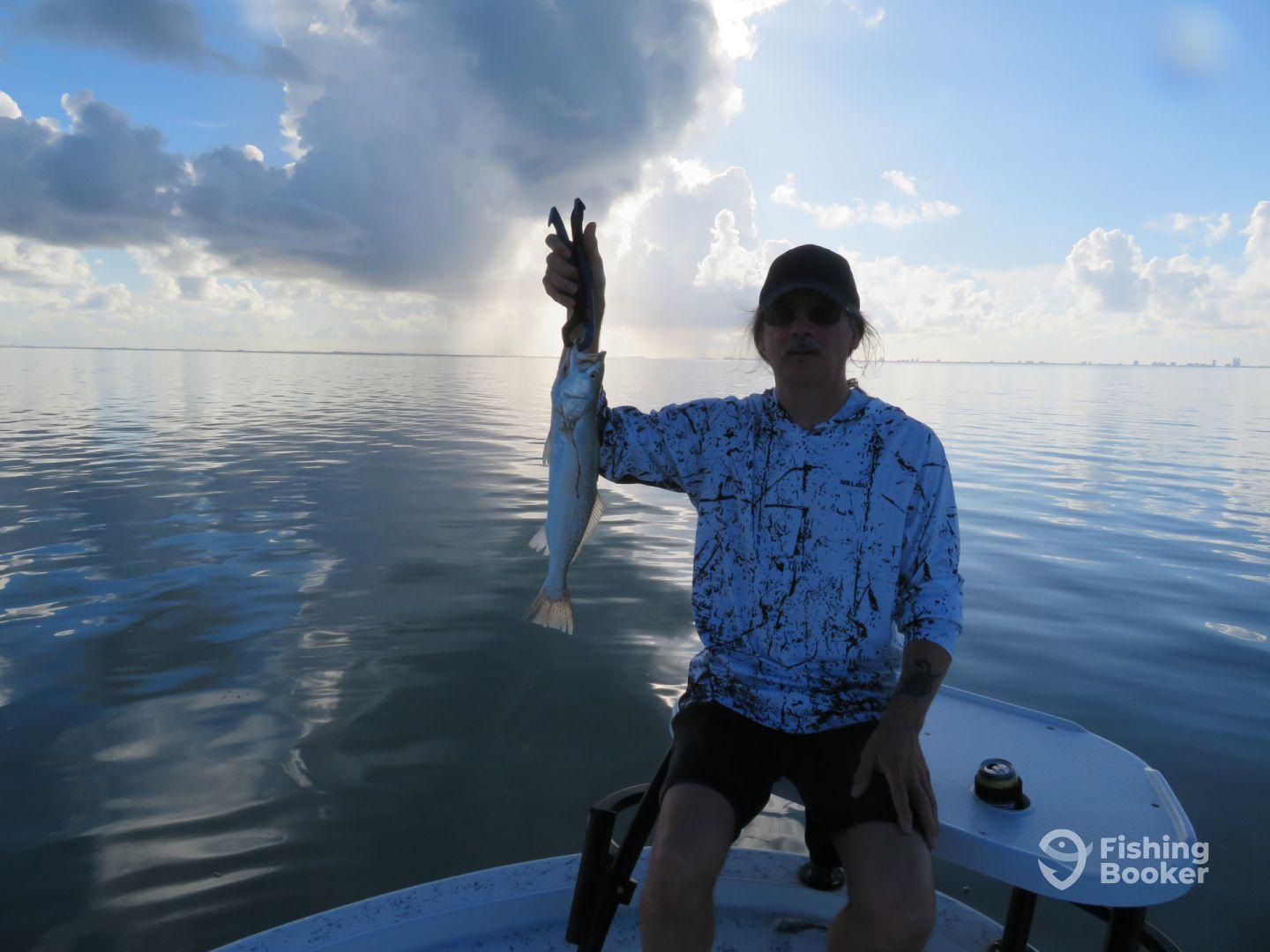 Angler proudly displaying a Speckled Trout while fishing on calm waters, showcasing a serene coastal environment.