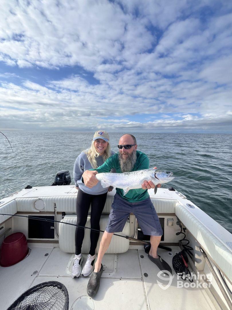 Two anglers proudly displaying a large Silver Salmon while fishing on a boat in open waters.