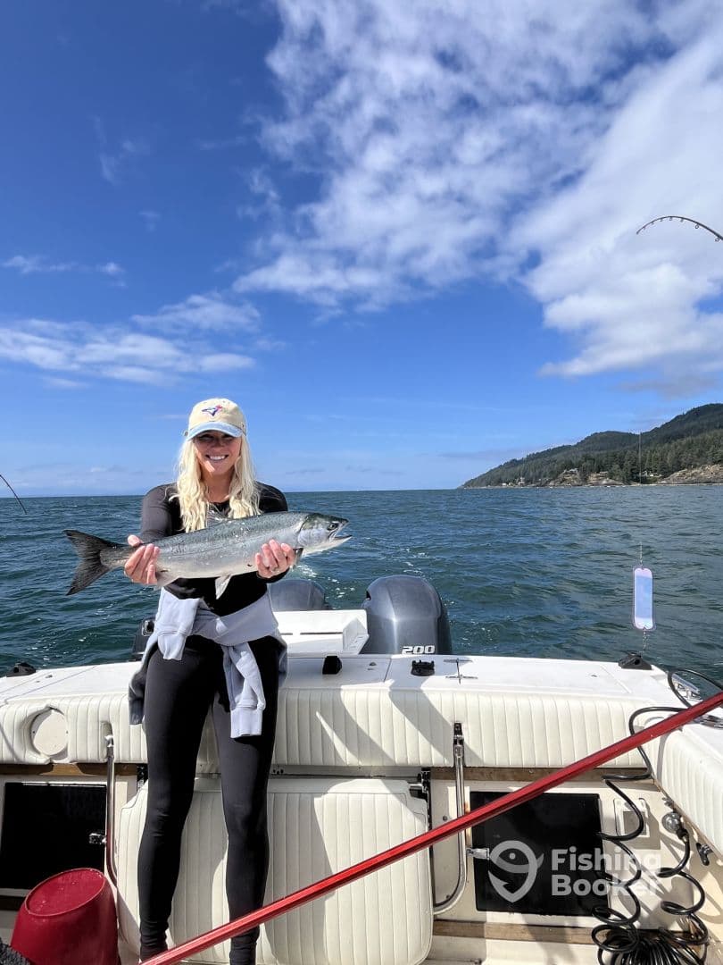 An angler proudly displaying a Silver Salmon while fishing on a boat in a scenic coastal environment.