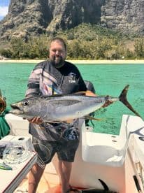 Angler proudly displaying a large Yellowfin Tuna aboard a boat in a tropical fishing environment.
