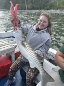 A young angler proudly displaying a striped bass while fishing on a boat, showcasing a fun day on the water.