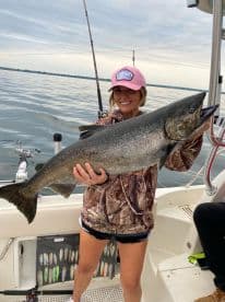 Angler proudly displaying a large Lake Trout while fishing on a boat, showcasing the serene waters of a freshwater lake.