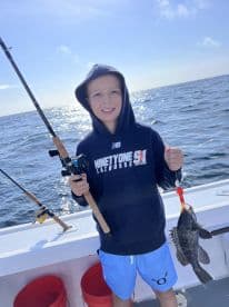 A young angler proudly displaying a caught fish while fishing on a boat, showcasing a sunny day on the water.