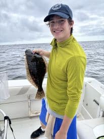 Young angler proudly holding a Flounder while fishing on a boat, showcasing a successful catch in a coastal environment.