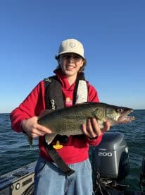 A young angler proudly displaying a large Walleye while fishing on a boat in clear waters.