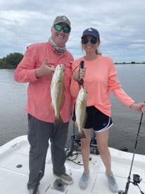 Two anglers proudly displaying their catch of Redfish while fishing on a calm day in a scenic waterway.