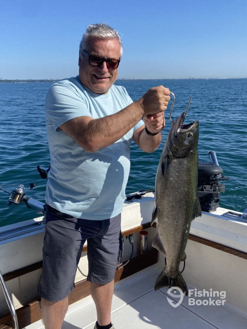 An adult angler proudly displaying a large Salmon while fishing on a boat, showcasing a successful day on the water.