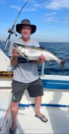 An angler proudly displaying a large Salmon while fishing on a boat in open waters.