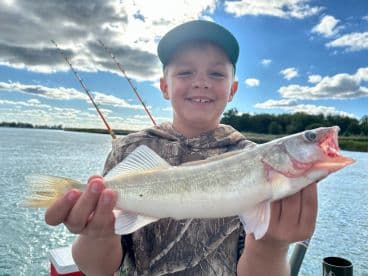 A young angler proudly displaying a freshly caught Walleye while fishing on a scenic river.