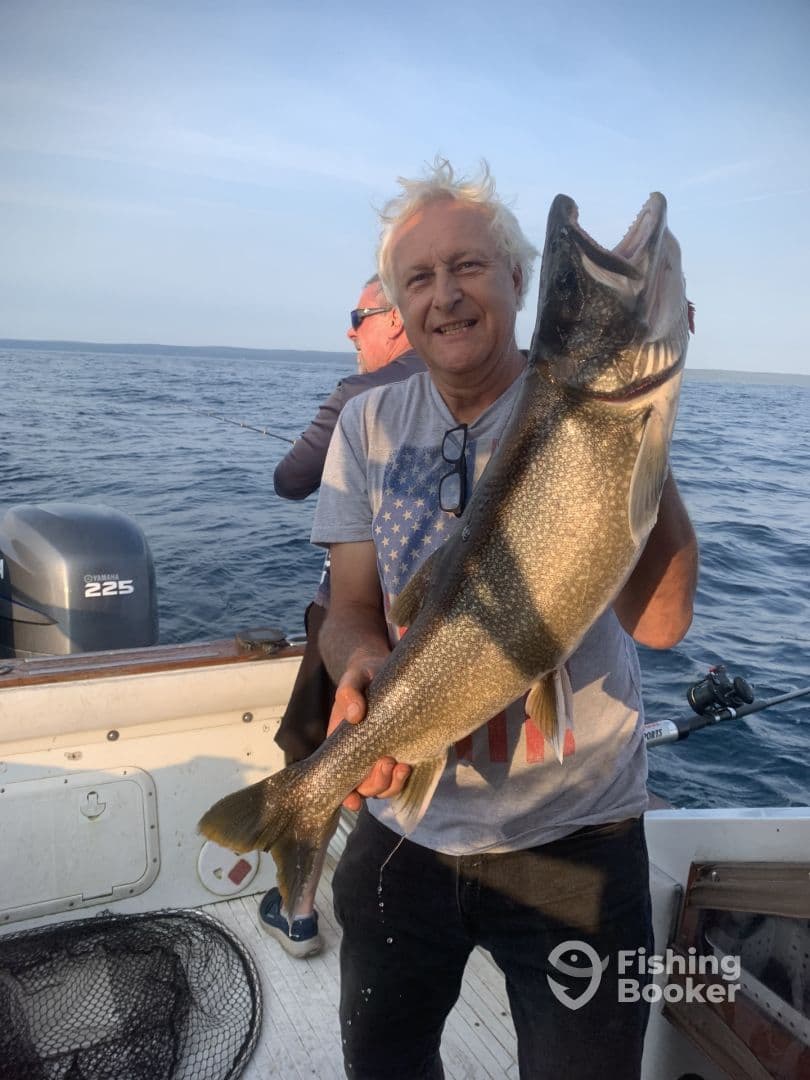 An angler proudly displaying a large Lake Trout while fishing on a boat, showcasing a successful day on the water.