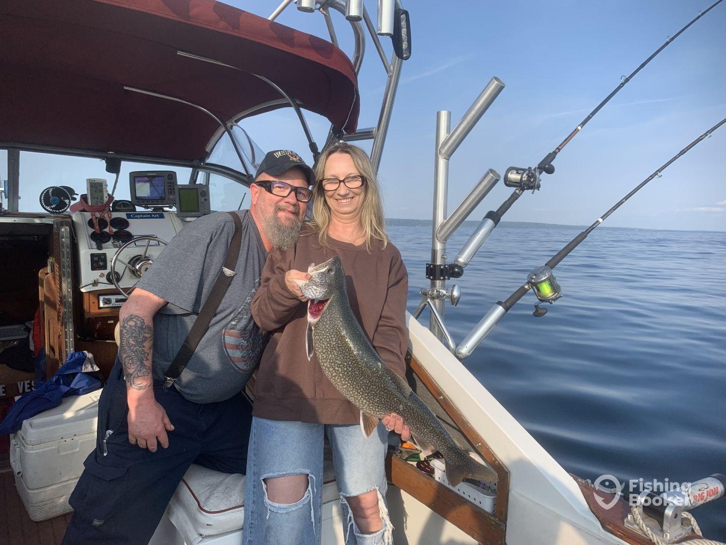Two anglers proudly displaying a large Lake Trout aboard a fishing boat, enjoying a day on the water.