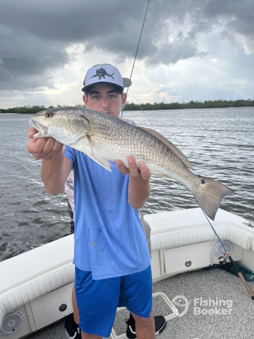 A young angler proudly displaying a large Redfish while fishing from a boat in a coastal waterway.