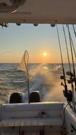 A scenic view from the back of a fishing boat during sunset, showcasing the ocean and fishing gear in action.
