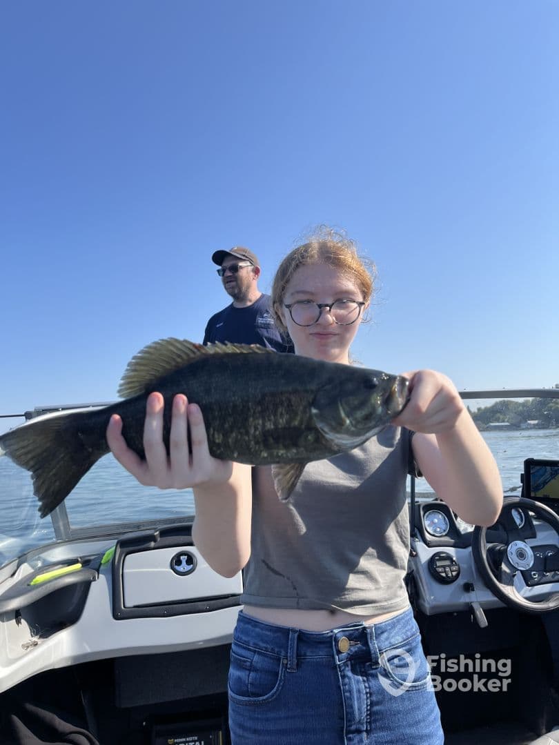 A young angler proudly displaying a large Largemouth Bass while fishing on a boat, enjoying a sunny day on the water.