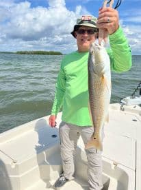 An angler proudly displays a large Redfish while fishing on a sunny day in a coastal waterway.