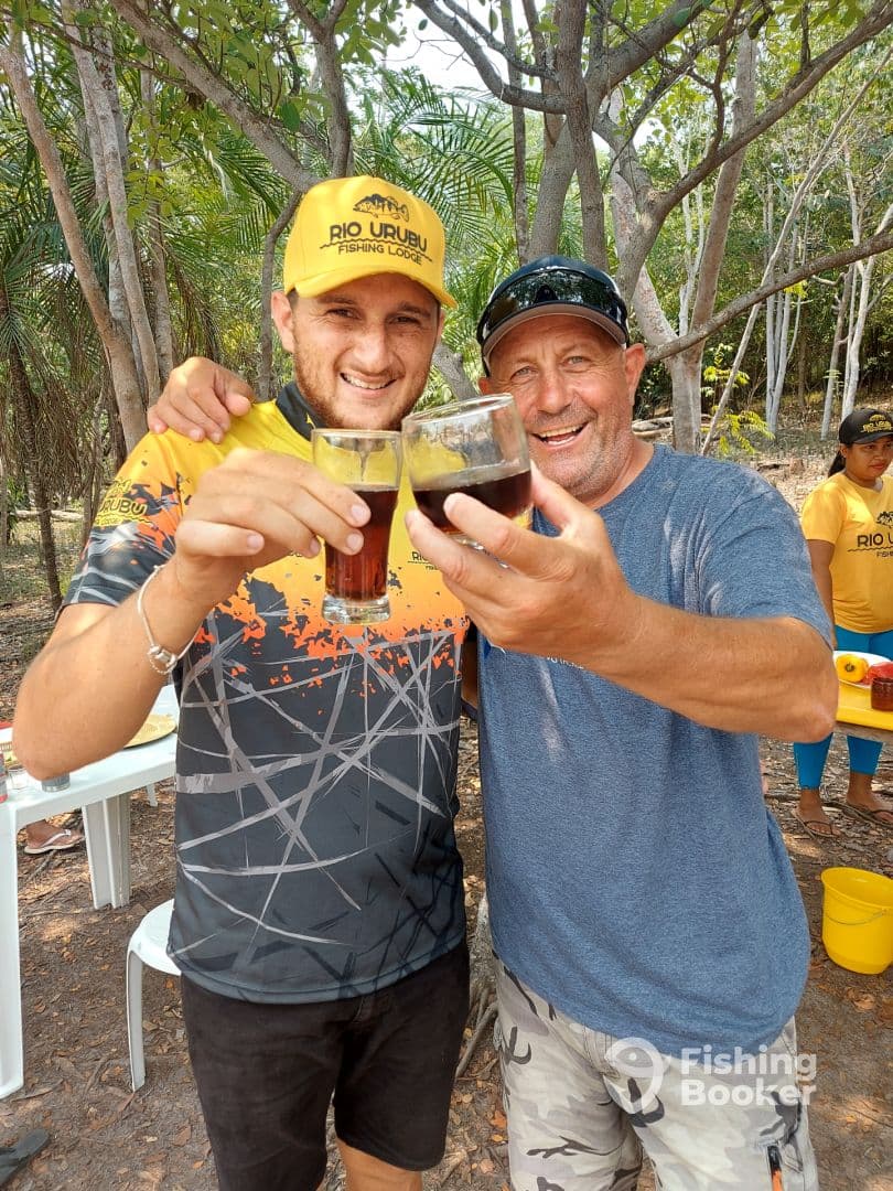 Two anglers celebrating with drinks in a tropical setting, likely after a fishing trip.