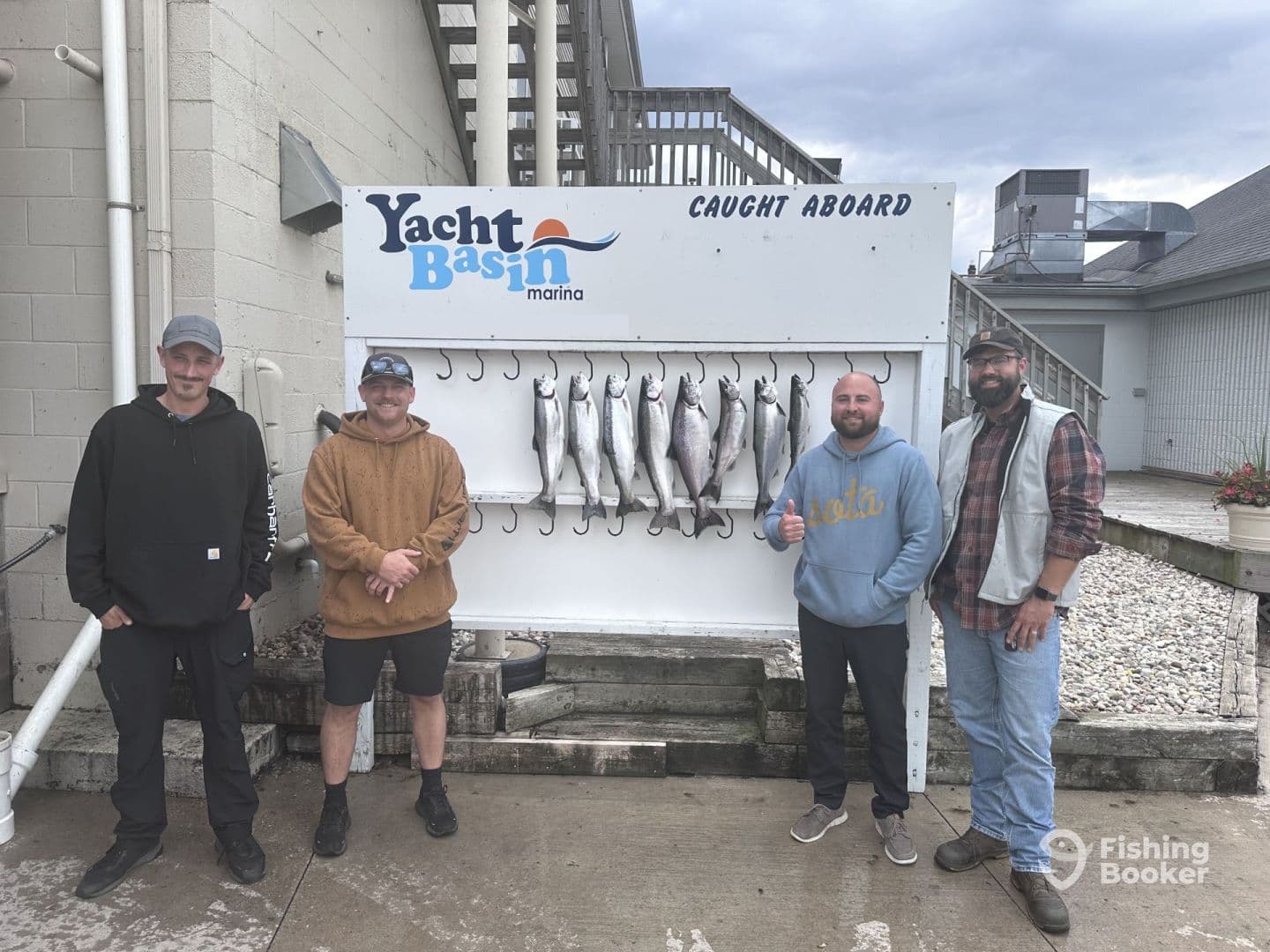 Group of four anglers proudly posing in front of a catch board displaying several fish after a successful fishing trip at Yacht Basin Marina.