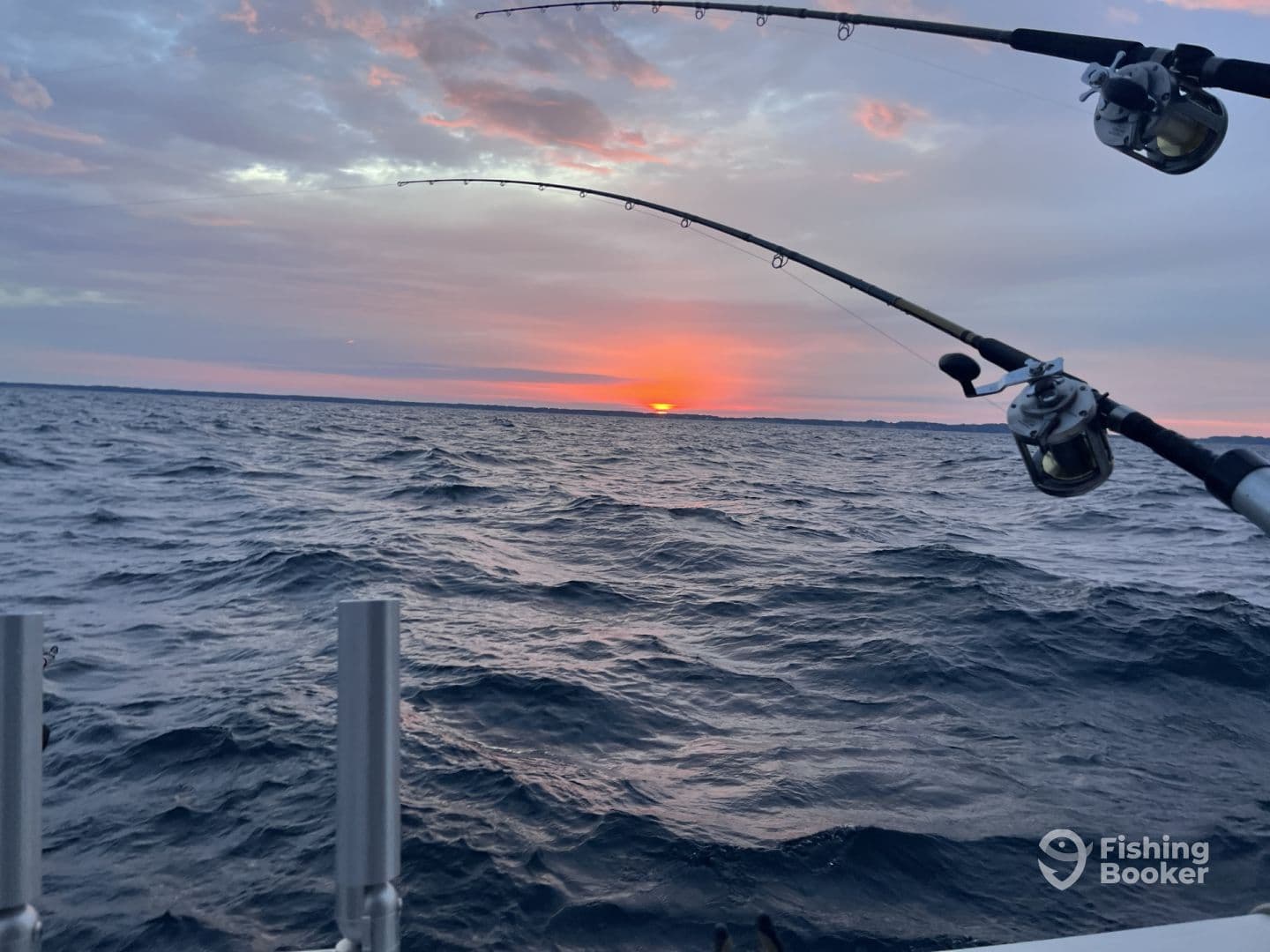 Fishing rods are positioned against a stunning sunset backdrop, capturing the essence of a tranquil evening on the water.