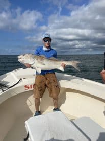 Angler proudly displaying a large Redfish while aboard a fishing boat, showcasing a successful day on the water.