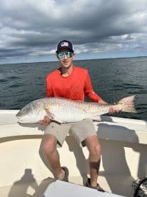 An angler proudly displaying a large Redfish while on a fishing trip, showcasing the excitement of a successful catch.