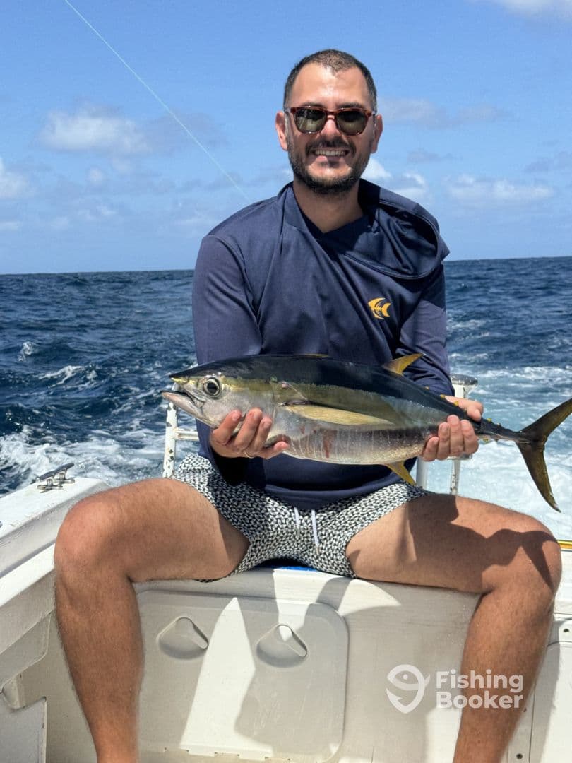 Angler proudly displaying a Yellowfin Tuna while seated on a boat in open waters, showcasing a successful offshore fishing trip.