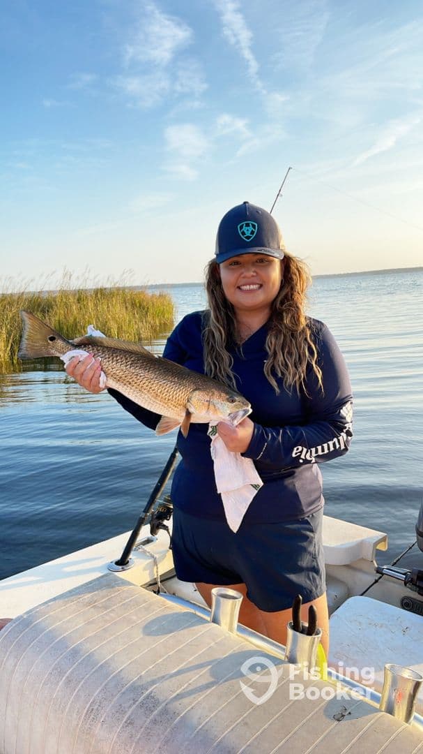 Angler proudly displaying a Redfish while fishing on a calm waterway, showcasing a successful day on the water.