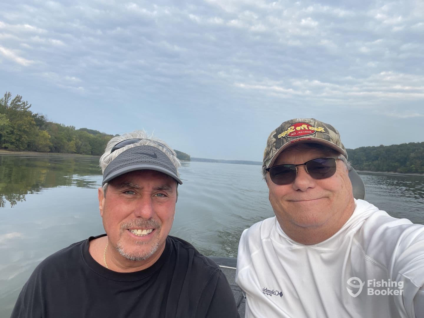 Two anglers enjoying a peaceful day on the water in a fishing boat, surrounded by lush greenery along the shoreline.