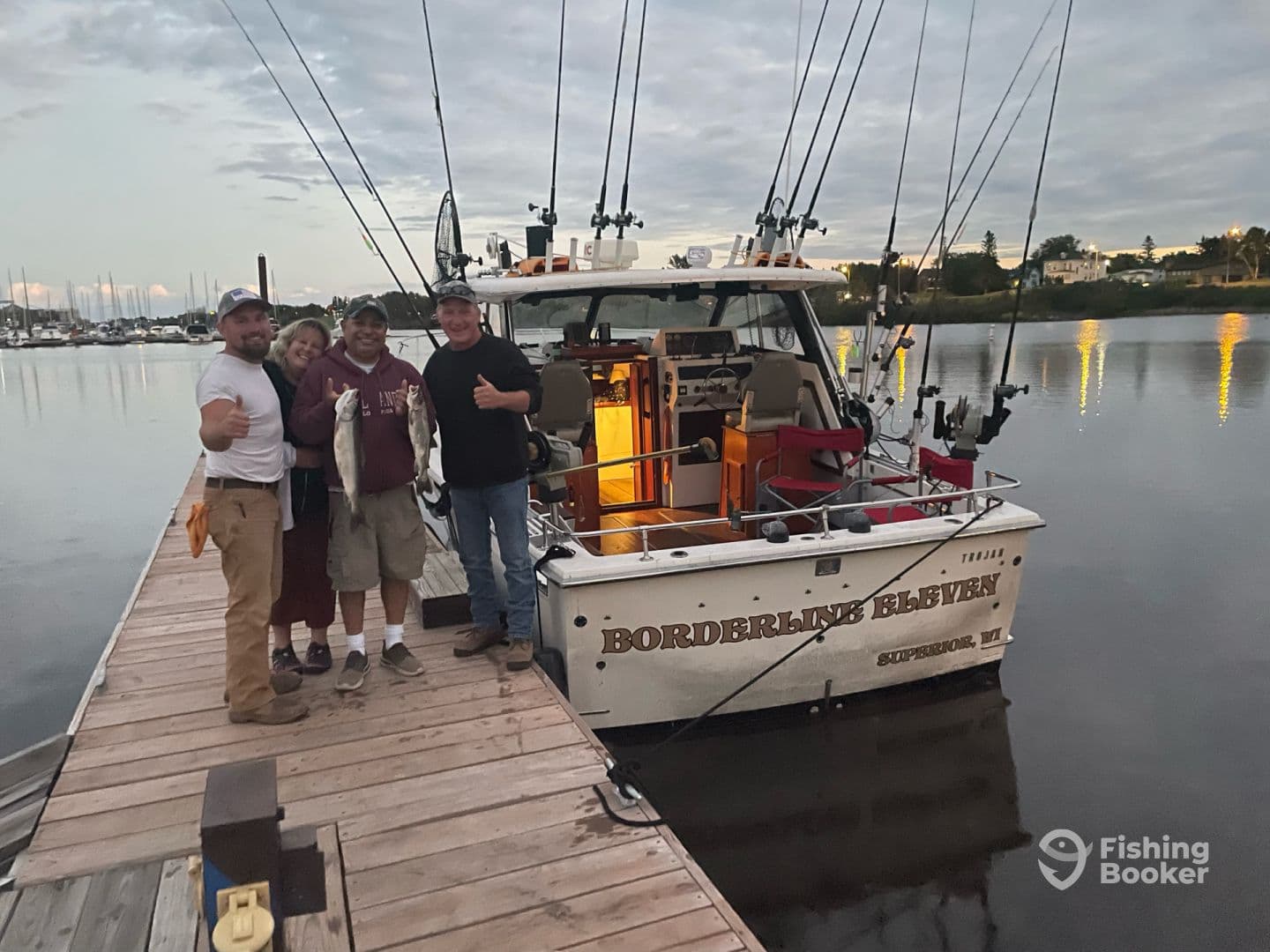 A group of four anglers proudly displaying their catch of two fish while standing on the dock next to the 'Borderline Eleven' boat, showcasing a successful fishing trip.