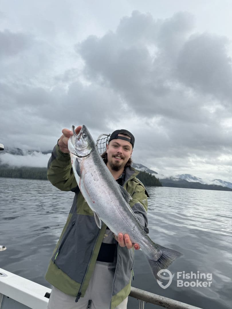Angler proudly displaying a large Silver Salmon while fishing in a scenic coastal environment.