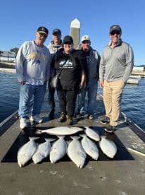 A group of five anglers proudly displaying their catch of several Halibut on a dock after a successful fishing trip.