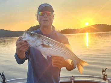 Angler holding a large Striped Bass during a sunset fishing trip on a calm lake.