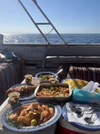 A beautifully arranged seafood feast on the deck of a fishing boat, featuring shrimp, fish, and fresh salad, set against a stunning ocean backdrop.